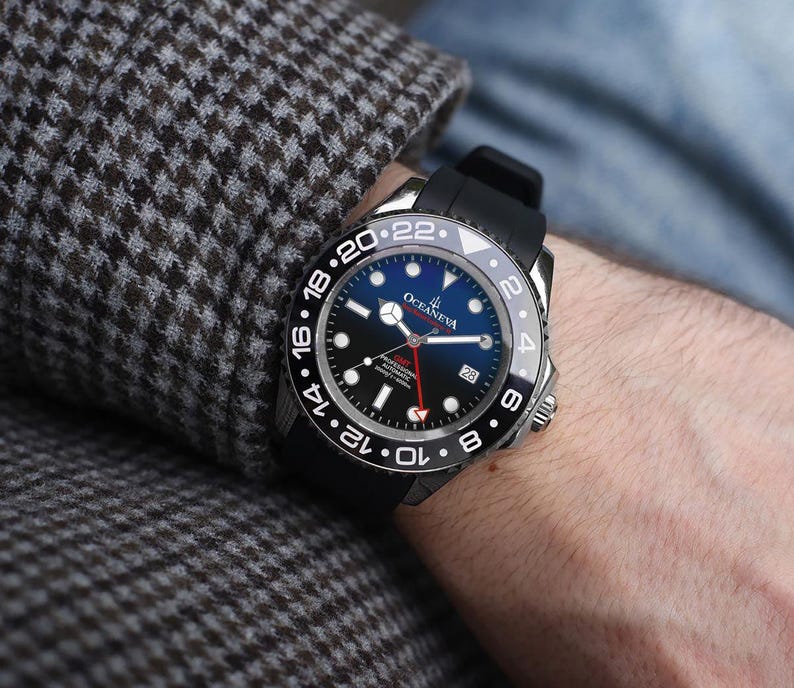 K&ouml;nnte beinhalten: Eine schwarze und silberne Armbanduhr mit blauem Zifferblatt und schwarzem Kautschukarmband. Die Uhr hat wei&szlig;e Ziffern und einen roten Sekundenzeiger. Die Uhr befindet sich am Handgelenk einer Person, mit einem Tweed-Jacken&auml;rmel im Hintergrund.