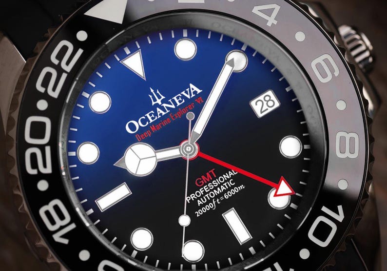 K&ouml;nnte beinhalten: Nahaufnahme einer schwarzen und blauen Oceaneva Deep Marine Explorer VI Uhr. Das Zifferblatt der Uhr hat wei&szlig;e Zeiger und Markierungen, ein Datumsfenster und den Text "GMT PROFESSIONAL AUTOMATIC 20000ft=6000m". Die L&uuml;nette hat wei&szlig;e Ziffern.