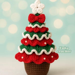 May include: A handmade crochet Christmas tree in red, green, and white, topped with a white star and a red bow. The tree is adorned with small white beads and sits on a brown base. The text "Xuka crochet" is visible on the right side.