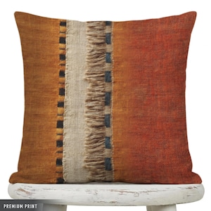 May include: A square throw pillow featuring a textured fabric with vertical color blocking in shades of burnt orange and mustard yellow. A central cream-colored panel is accented with frayed fringe detailing and thin black vertical stripes.