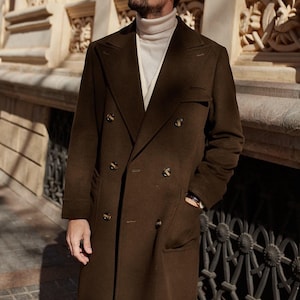 May include: A dark brown double-breasted wool coat with wide lapels and six buttons, worn over a cream-colored ribbed turtleneck sweater. The coat features long sleeves, two side pockets, and a structured fit with a classic tailored silhouette.