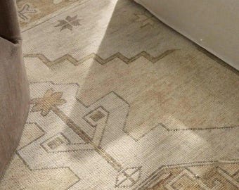 May include: A rectangular area rug featuring a light beige and tan color palette with a repeating geometric pattern. The design includes stylized star motifs and angular, zigzagging lines woven into the fabric, creating a textured surface.
