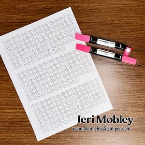May include: A white sheet with numerous small, circular labels, each containing text, lies on a wooden surface. Two pink and black markers labeled "Strawberry Slush" are positioned nearby. The image also includes the text "Jeri Mobley" and "www.ShamelessStamper.com".