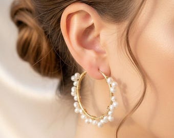 May include: Gold hoop earrings adorned with small, white pearls. The earrings are a classic design, featuring a circular shape with the pearls evenly spaced around the outer edge. The gold setting provides a warm contrast to the bright pearls.