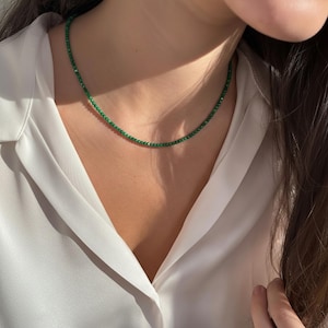 Peut inclure: Un délicat collier de perles vertes. Le collier est composé de petites perles rondes, créant un fil continu. Le collier est porté sur une chemise blanche.