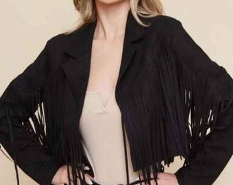 May include: Black cropped jacket with fringe detailing. The jacket features a classic collar and long fringe along the sleeves and front. The model is wearing a beige top and black pants. The jacket is a stylish outerwear piece.