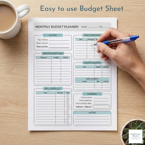 May include: A white monthly budget planner with teal accents, featuring sections for income, expenses, and savings. The text "Easy to use Budget Sheet" is at the top. A hand is holding a pen over the planner.