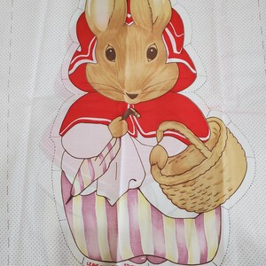 May include: A fabric panel featuring a printed illustration of Mrs. Bunny from Beatrix Potter Nursery Classics. The character wears a red cape and holds a basket and umbrella. The white background has a subtle dot pattern and includes the text Mrs. Bunny, Beatrix Potter Nursery Classics, and Leave open for stuffing.
