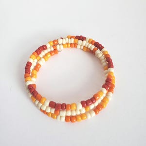 May include: A beaded wrap bracelet featuring three strands of small, colorful beads. The bracelet's color palette includes shades of red, orange, yellow, and white. The bracelet is designed to wrap around the wrist multiple times.