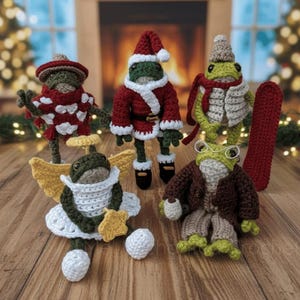Op de afbeelding: Een promotieafbeelding voor gehaakte winteroutfits voor Pebble the Pocket Frog. De afbeelding toont vijf kikkerfiguren gekleed in verschillende winterthema-outfits, waaronder een kerstmanpak en engelen vleugels. De tekst luidt "ADD-ON WINTER OUTFITS FOR PEBBLE THE POCKET FROG".