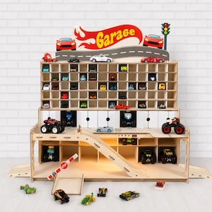 Può includere: Garage giocattolo in legno con più scomparti per macchinine. Il garage presenta una rampa, un segnale di stop e un'insegna con la scritta "Garage". La parte superiore del garage ha un design stradale con macchinine rosse e un semaforo.