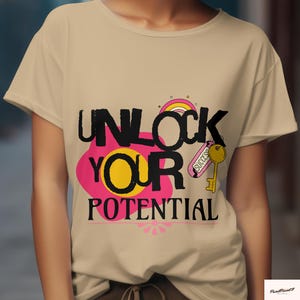 Könnte beinhalten: Beiges T-Shirt mit dem Schriftzug "UNLOCK YOUR POTENTIAL" in Schwarz, Pink und Gelb. Das Design beinhaltet einen Schlüssel, einen Regenbogen und eine rosa Blume. Das T-Shirt hat kurze Ärmel.