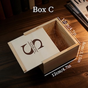 May include: A wooden box with a sliding lid, measuring 4.7 inches by 4.7 inches and 3.15 inches tall. The lid is engraved with the name "SIMON" and a large letter "S". The box is open, revealing a straw-like filler.