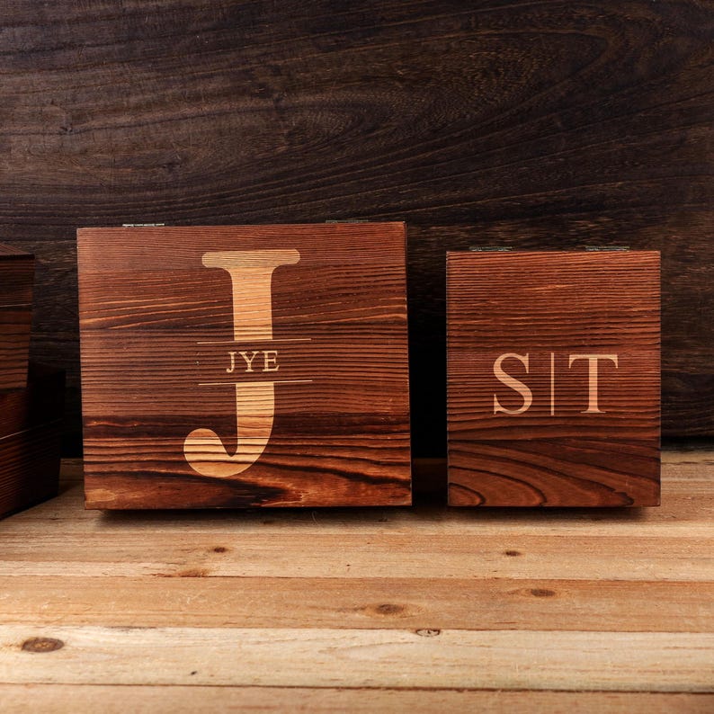 May include: Two wooden boxes with a dark brown finish. The larger box has a large letter "J" with "JYE" underneath. The smaller box has the letters "SIT". Both boxes are on a wooden surface.