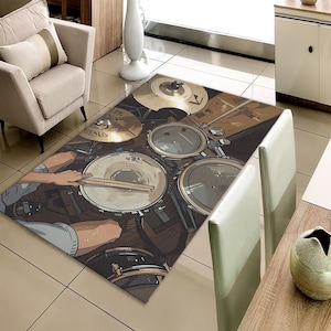 Op de afbeelding: Een rechthoekig vloerkleed met een drumstel illustratie. Het vloerkleed toont een drumstel met bekkens, drums en drumstokken. Het ontwerp heeft een bruin en beige kleurenschema, met een cartoonstijl.