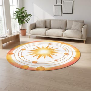 May include: A round rug featuring a celestial design. The rug has a white center with a bright yellow sunburst design. Orange planets and rings surround the sun, with a gradient orange and pink border. The rug is placed on a light wood floor.