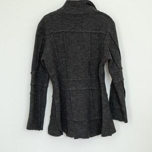 Peut inclure: Un manteau en laine gris fonc&eacute; avec un col montant et des manches longues. Le manteau a une coupe ajust&eacute;e avec des coutures et un bas &eacute;vas&eacute;. Il est suspendu &agrave; un cintre en m&eacute;tal sur fond blanc.
