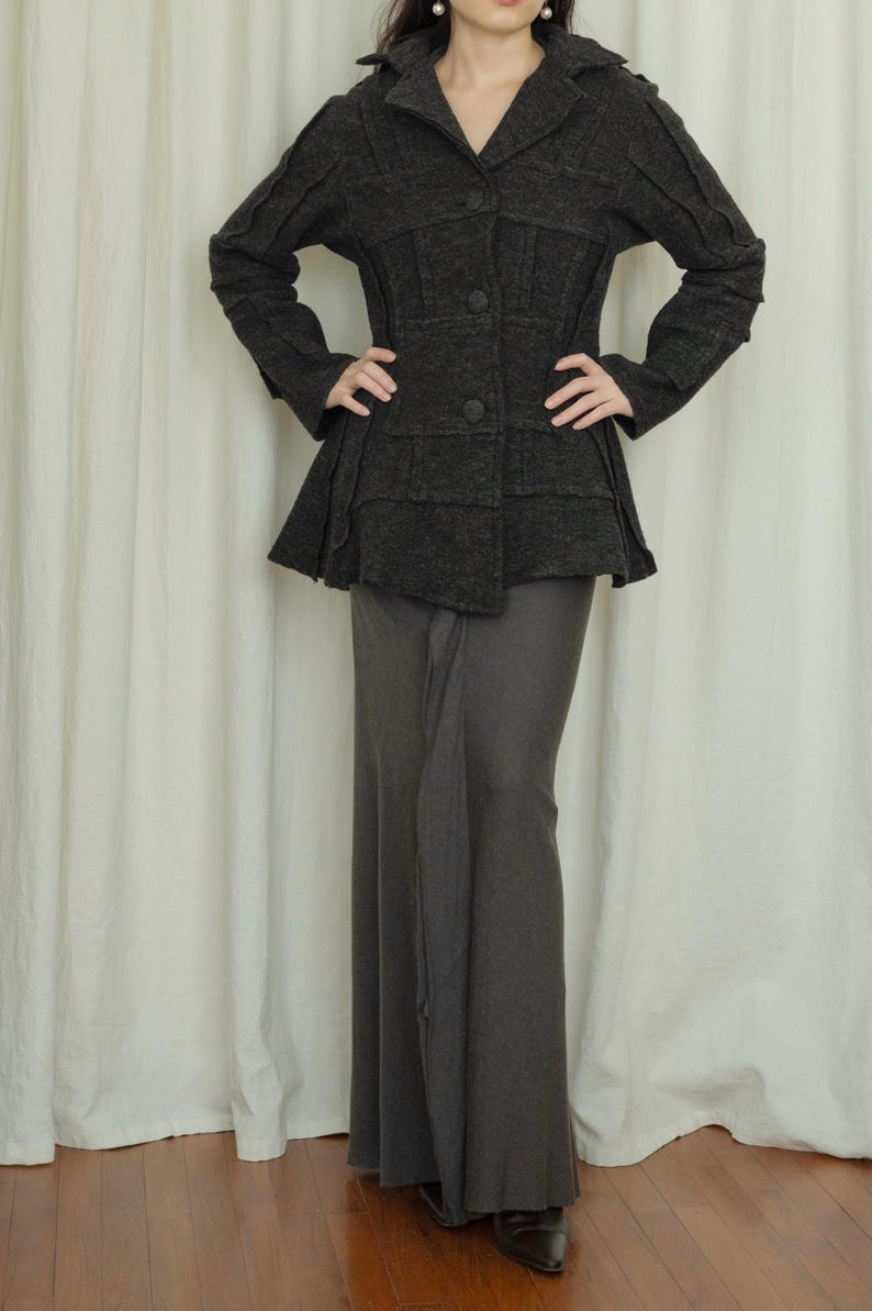 Peut inclure: Veste gris fonc&eacute; avec un corsage ajust&eacute; et un basque &eacute;vas&eacute;, associ&eacute;e &agrave; une longue jupe assortie. La veste pr&eacute;sente un col crant&eacute; et des boutons. L'ensemble est monochrome.
