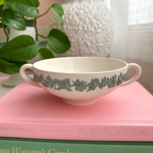 May include: A white ceramic mug with a black handle and the text "But First, Coffee" in a bold, black font. The mug is sitting on a wooden surface. The mug is 4 inches tall.