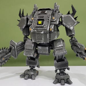 May include: A gray mechanical robot figure with a weathered finish, featuring a large circular saw blade on its right arm and a multi-barreled cannon on its left arm. The torso has a central yellow light, and the armor plates are detailed with rivets.