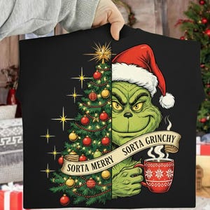 May include: Black t-shirt featuring a Christmas tree on the left and the Grinch wearing a Santa hat on the right. The Grinch is holding a red mug with a snowflake design. The banner reads "Sorta Merry Sorta Grinchy."