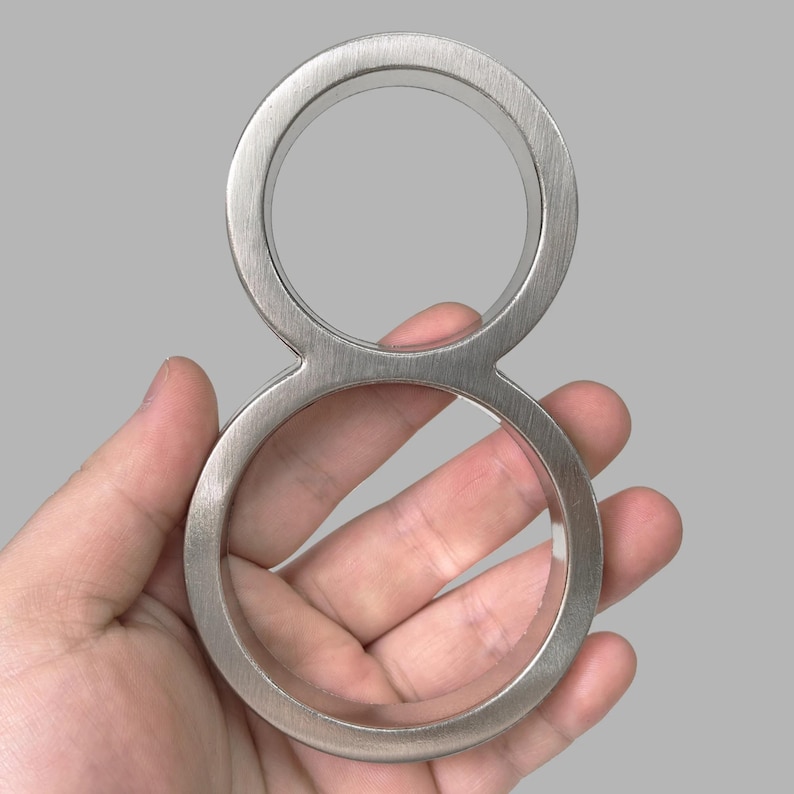 May include: A brushed metal number eight. The number is held in a hand. The number is made of a single piece of metal with a brushed finish. The number is a decorative item.