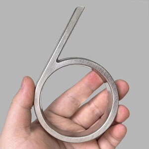 May include: A brushed metal number six, held in a hand. The number has a modern, minimalist design with a circular base and a straight top. The metal has a textured finish.