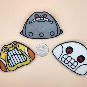 Puede incluir: Tres objetos con forma de cara de estilo caricatura con expresiones de enfado. Uno es gris, otro amarillo y naranja, y el otro blanco. Una moneda de veinticinco centavos estadounidense está entre ellos. Los objetos tienen contornos negros y ojos rojos.