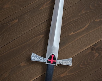 May include: A silver-colored sword with a pointed blade and a black handle. The crossguard features a red cross on a shield. The hilt has a red gem at the end. The sword is set against a dark wood background.