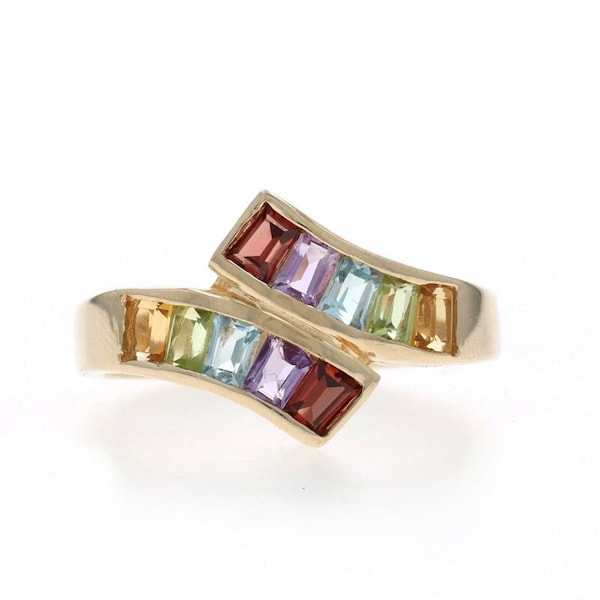 Puede incluir: Un anillo de oro tipo bypass con dos filas paralelas de piedras preciosas en corte baguette. Cada fila contiene cinco piedras en un degradado de colores que incluye rojo, morado, azul claro, verde y amarillo, engastadas en una banda de oro pulido.