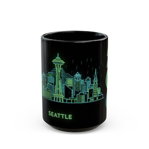 May include: Black ceramic mug featuring a neon green and blue illustration of the Seattle skyline, including the Space Needle and city buildings. The word "SEATTLE" is printed in green at the bottom of the mug.