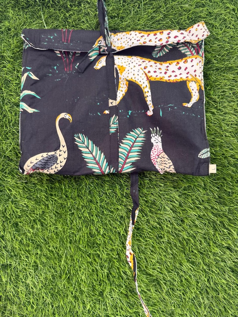 以下が含まれることがあります： フラミンゴ、ヒョウ、オウムが描かれた、カラフルなジャングルプリントの黒い布製バッグ。バッグには白いトリムと紐留めが付いています。背景は緑色です。