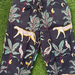 以下が含まれることがあります： ジャングルをテーマにしたプリントの黒いパジャマパンツ。ヒョウ、オウム、ヤシの木、その他の熱帯要素が含まれています。パンツはドローストリングウエストで、軽量の生地で作られています。