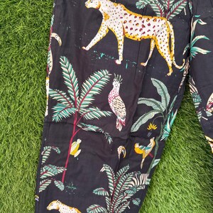 以下が含まれることがあります： 黒色の生地に、ヒョウ、オウム、ヤシの木がプリントされています。ヒョウには黄色とオレンジ色の斑点があります。オウムは白、黄色、赤です。ヤシの木には緑と赤の葉があります。