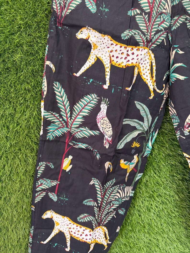 以下が含まれることがあります： 黒色の生地に、ヒョウ、オウム、ヤシの木がプリントされています。ヒョウには黄色とオレンジ色の斑点があります。オウムは白、黄色、赤です。ヤシの木には緑と赤の葉があります。