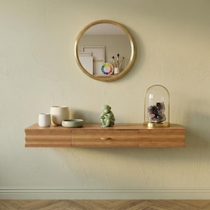 May include: A wooden floating shelf with two drawers, adorned with decorative items. A round gold mirror hangs above, reflecting a color wheel and art supplies. The shelf displays a green monkey figurine, a small bowl, and a glass cloche with a purple crystal.