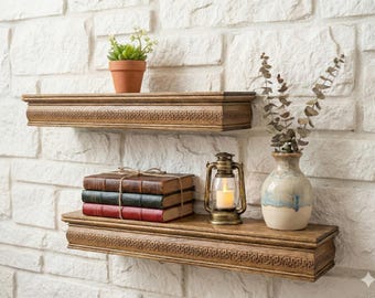 Può includere: Due mensole in legno con bordi decorativi sono montate su un muro di mattoni bianchi. La mensola superiore contiene una piccola pianta in vaso. La mensola inferiore mostra libri impilati, una lanterna e un vaso con steli secchi.