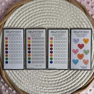Peut inclure: Quatre cartes rectangulaires avec le texte "Kleurenspel" et des graphiques colorés. Chaque carte présente une grille de carrés et de cercles colorés, avec du texte et des symboles d'euros. Les cartes sont disposées sur un tapis tissé.