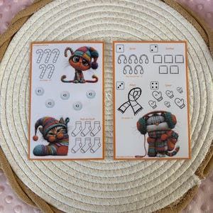 Puede incluir: Dos tarjetas de juego rectangulares con ilustraciones coloridas de gatitos con accesorios de invierno. La tarjeta izquierda muestra bastones de caramelo, círculos de monedas y calcetines. La derecha muestra iconos de dados, auriculares, una bufanda y manoplas.