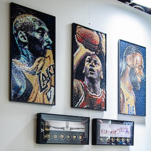 以下が含まれることがあります： 小さなカラフルなブロックで細心の注意を払って作られた、額入りのポートレートのコレクション。ポートレートは、バスケットボール選手やスターウォーズのキャラクターなど、有名なアスリートやポップカルチャーのアイコンを描いています。アートワークは白い壁に展示されています。
