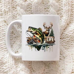 Może przedstawiać: Biały ceramiczny kubek z kolorową ilustracją skaczącego bass'a wielkogębowego, jelenia i napisem "HUNTING LIFE". Kubek ma biały uchwyt i jest umieszczony na teksturowanym białym tle.