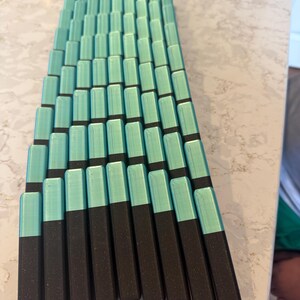 May include: A collection of rectangular objects, arranged in a fan-like pattern. Each object is a combination of two colors: a teal top and a dark brown base. The objects are neatly aligned, creating a visually appealing geometric design.