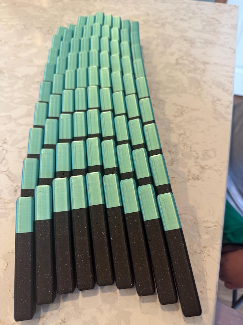 May include: A collection of rectangular objects, arranged in a fan-like pattern. Each object is a combination of two colors: a teal top and a dark brown base. The objects are neatly aligned, creating a visually appealing geometric design.