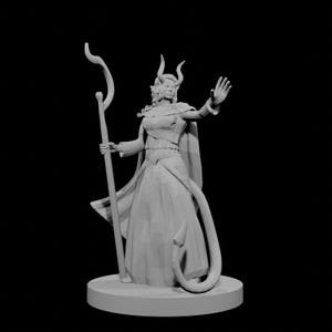 以下が含まれることがあります： 角、長い尻尾、杖を持つ女性ファンタジーキャラクターの灰色の3Dプリントフィギュア。長いドレスとケープを着ており、片手を上げています。フィギュアは円形の台座の上に立っています。