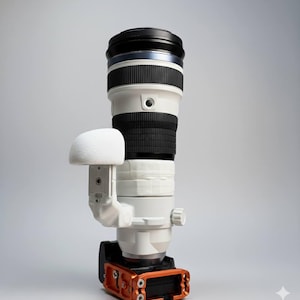 May include: A white and black telephoto camera lens with a white lens hood and an orange base. The lens has a black top and a white body with black bands. The lens hood is white and attached to the side. The base is orange.