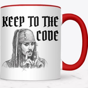 May include: White ceramic mug with a red interior and handle. The mug features a black and white illustration of a character with the text "KEEP TO THE CODE".