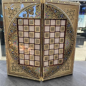 May include: A decorative, hinged wooden box with a detailed, colourful design. The box features a chessboard pattern on the inside and intricate floral and geometric patterns on the exterior, with gold and brown tones.