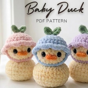 Peut inclure: Trois canetons au crochet faits à la main, avec des corps jaunes, des becs oranges et des yeux noirs. Chaque caneton porte un chapeau aux couleurs pastel avec des accents de feuilles vertes. Le texte "Baby Duck PDF PATTERN" est en haut.