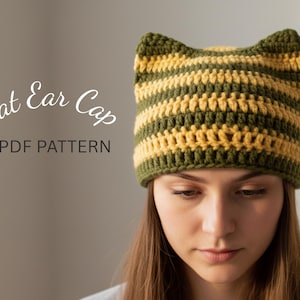 Può includere: Un cappello all'uncinetto con orecchie da gatto a righe verdi oliva e gialle. Il cappello è indossato da una persona. Il testo "Cat Ear Cap PDF Pattern" è visualizzato sul lato sinistro dell'immagine.