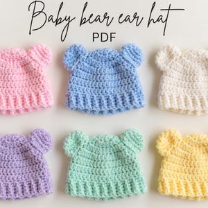 May include: Six crocheted baby bear ear hats in pastel colors: pink, blue, white, purple, mint green, and yellow. The hats are handmade with a ribbed brim and bear ears on top. The text "Baby bear ear hat PDF" is written in cursive at the top.